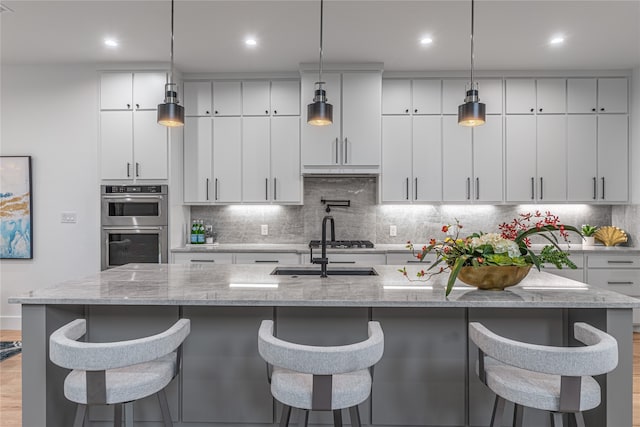 kitchen featuring light stone countertops, an island with sink, and decorative light fixtures