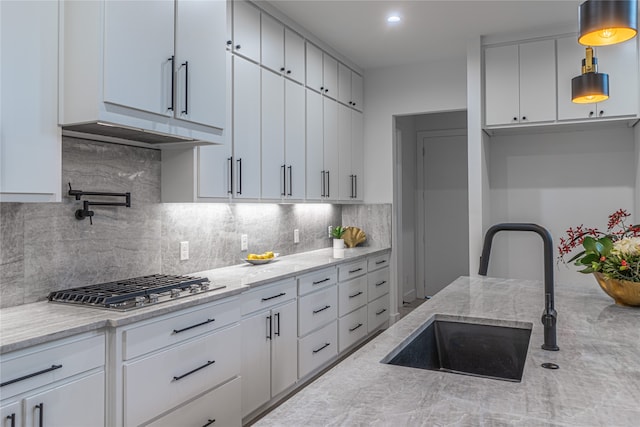 kitchen featuring tasteful backsplash, sink, hanging light fixtures, white cabinets, and light stone counters