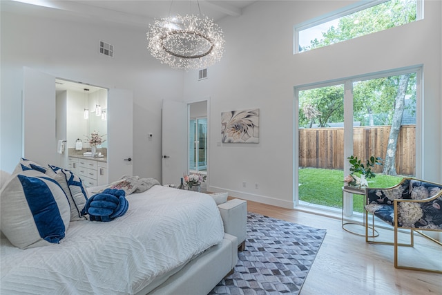 bedroom featuring beam ceiling, connected bathroom, a high ceiling, light hardwood / wood-style floors, and a notable chandelier