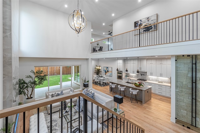 living room featuring ceiling fan with notable chandelier, a high ceiling, and light wood-type flooring