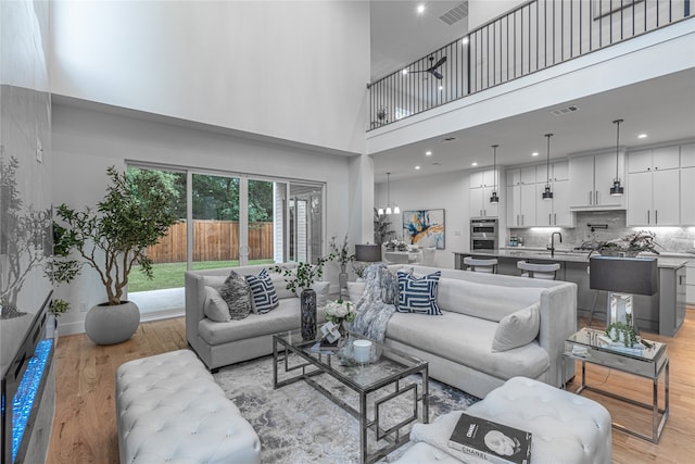 living room with a chandelier, sink, a high ceiling, and light wood-type flooring