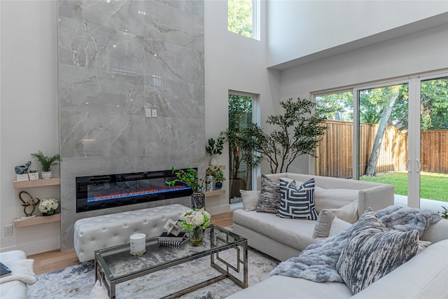 living room featuring a tiled fireplace, hardwood / wood-style flooring, a wealth of natural light, and a high ceiling