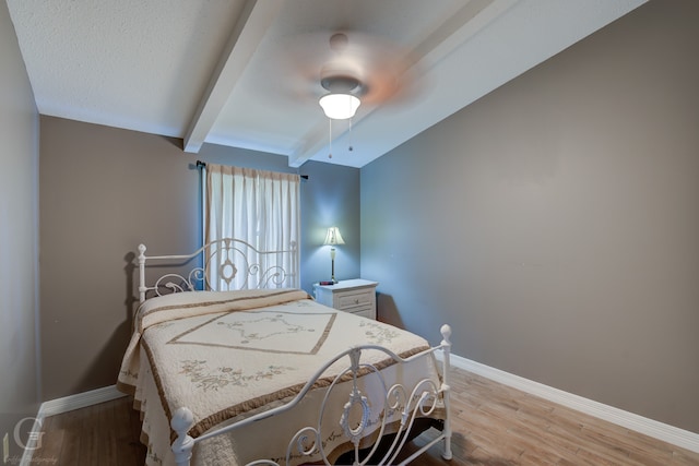 bedroom featuring light wood-type flooring, ceiling fan, and vaulted ceiling with beams