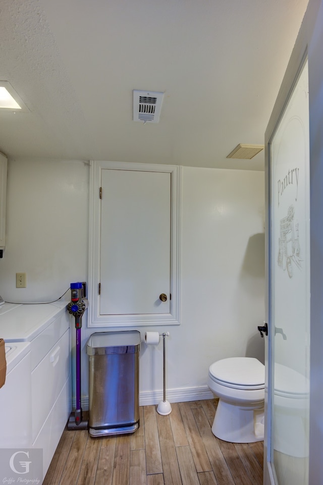 bathroom with toilet, independent washer and dryer, and hardwood / wood-style flooring