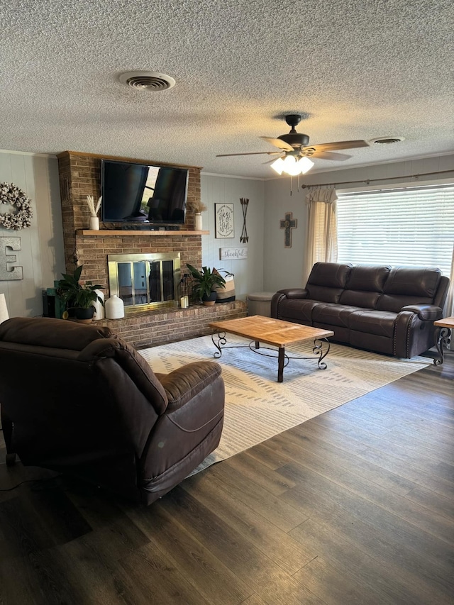 living room with a brick fireplace, ceiling fan, hardwood / wood-style flooring, and a textured ceiling