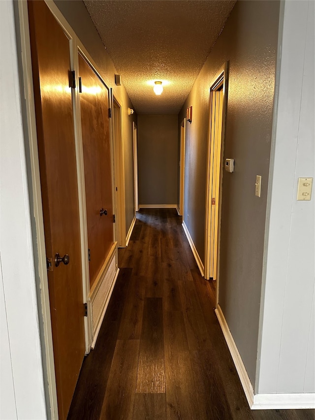 hallway with a textured ceiling and dark hardwood / wood-style flooring