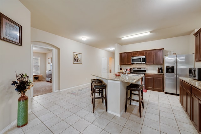 kitchen with light colored carpet, light stone countertops, appliances with stainless steel finishes, and decorative backsplash