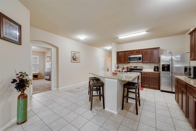 2512 Saldana Dr, Fate, TX 75189 - kitchen with appliances with stainless steel finishes, light tile patterned flooring, arched walkways, and a kitchen bar