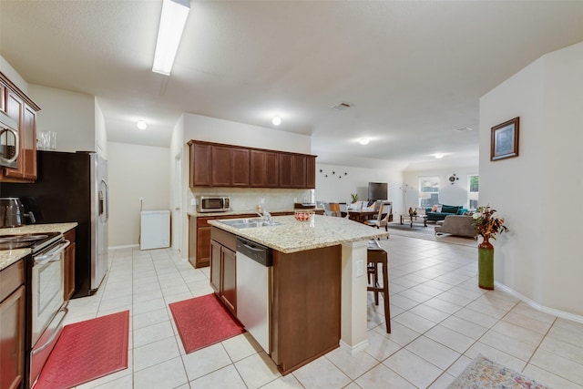 2512 Saldana Dr, Fate, TX 75189 - kitchen featuring appliances with stainless steel finishes, light tile patterned flooring, open floor plan, and a center island with sink