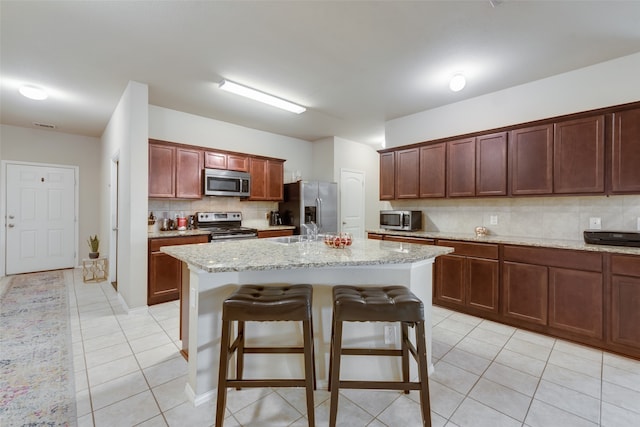 kitchen with an island with sink, stainless steel appliances, light tile patterned flooring, and tasteful backsplash