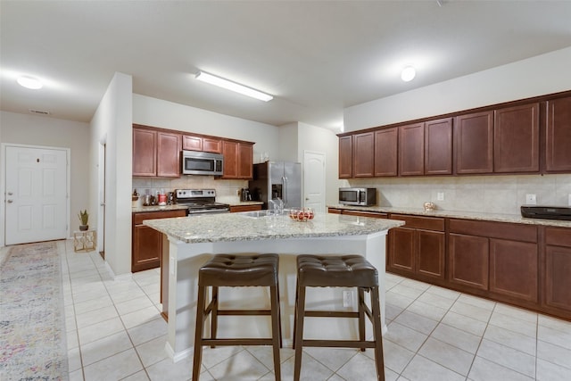 2512 Saldana Dr, Fate, TX 75189 - kitchen with appliances with stainless steel finishes, light tile patterned floors, tasteful backsplash, a breakfast bar, and a center island with sink