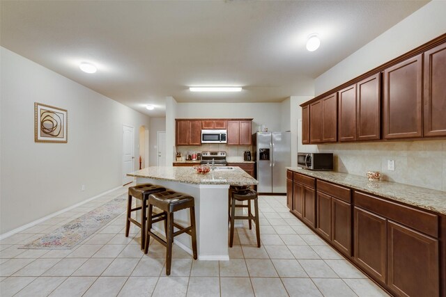 2512 Saldana Dr, Fate, TX 75189 - kitchen with appliances with stainless steel finishes, backsplash, a kitchen bar, light tile patterned floors, and light stone countertops