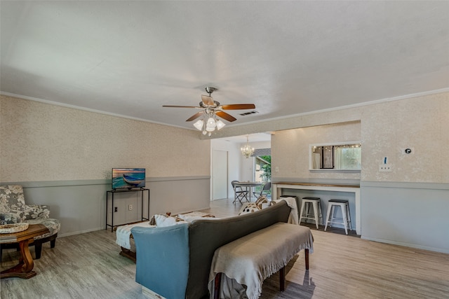 living room with ceiling fan with notable chandelier, light hardwood / wood-style floors, and ornamental molding