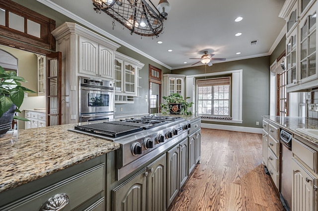 kitchen featuring crown molding, light wood-type flooring, appliances with stainless steel finishes, light stone counters, and ceiling fan