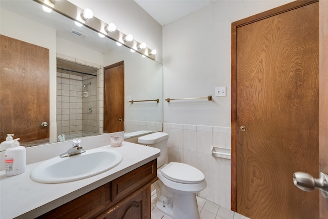 bathroom featuring toilet, tile patterned flooring, vanity, a tile shower, and tile walls