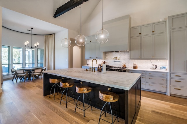 kitchen featuring high vaulted ceiling, tasteful backsplash, a kitchen island with sink, and hanging light fixtures