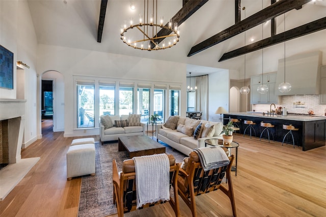 living room featuring sink, high vaulted ceiling, beam ceiling, and light hardwood / wood-style flooring