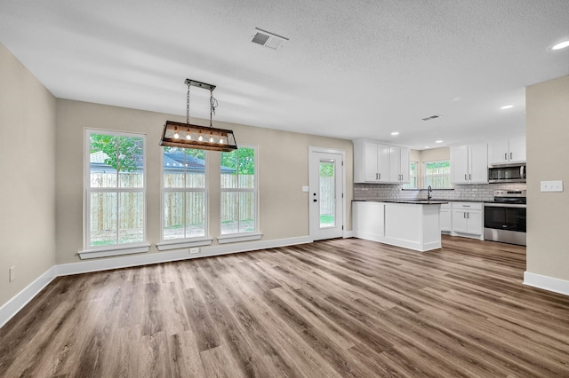 kitchen with hardwood / wood-style floors, white cabinetry, stainless steel appliances, decorative light fixtures, and sink