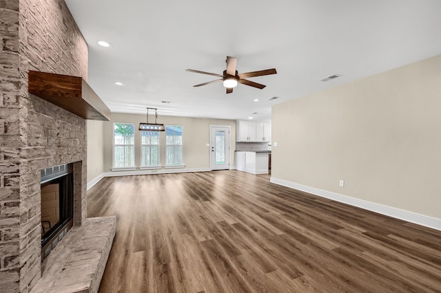 unfurnished living room featuring a fireplace, dark hardwood / wood-style flooring, and ceiling fan