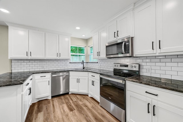 kitchen with tasteful backsplash, stainless steel appliances, sink, white cabinetry, and light wood-type flooring