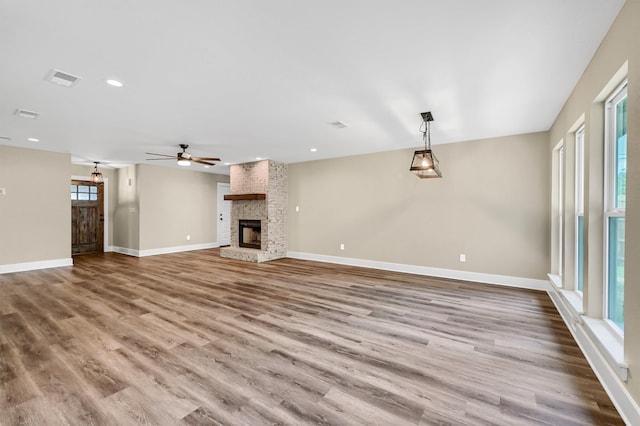 unfurnished living room with a healthy amount of sunlight, wood-type flooring, and a stone fireplace