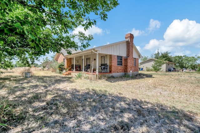 rear view of property featuring covered porch, brick siding, and a chimney