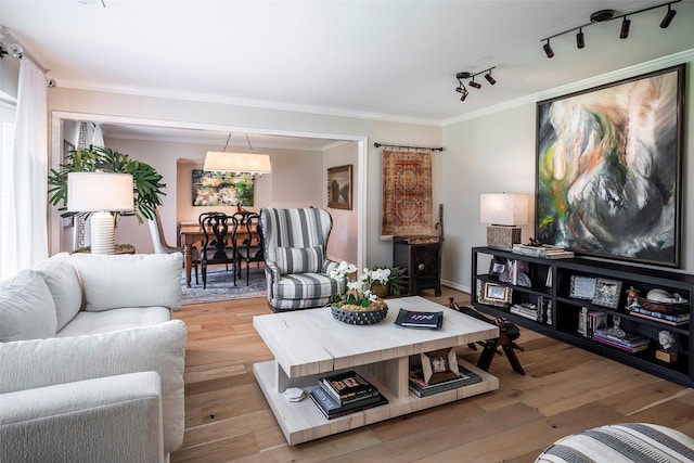 living room featuring rail lighting, crown molding, a notable chandelier, and light wood-type flooring