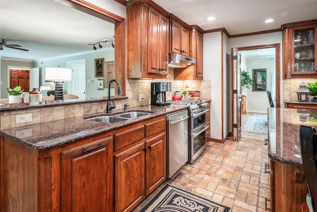 kitchen with stainless steel appliances, dark stone countertops, decorative backsplash, sink, and ornamental molding