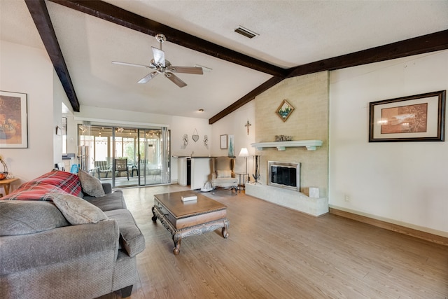 living room with light wood-type flooring, a textured ceiling, ceiling fan, lofted ceiling with beams, and a fireplace