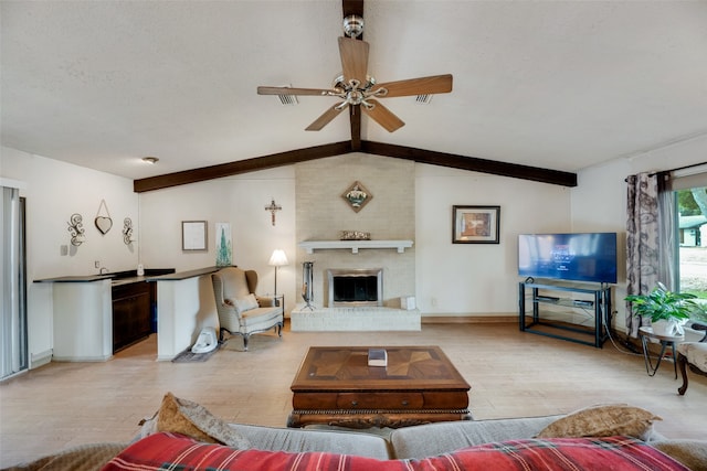 living room with vaulted ceiling with beams, ceiling fan, a fireplace, and light wood-type flooring