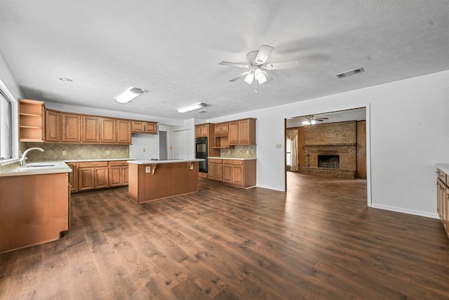 kitchen with a fireplace, backsplash, a kitchen island, ceiling fan, and dark wood-type flooring