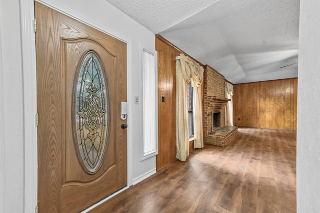 foyer featuring a fireplace, dark hardwood / wood-style flooring, wooden walls, and a textured ceiling