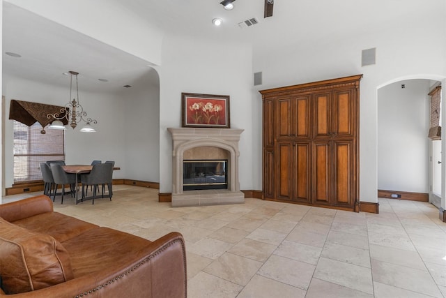 living area featuring arched walkways, visible vents, a towering ceiling, a high end fireplace, and baseboards