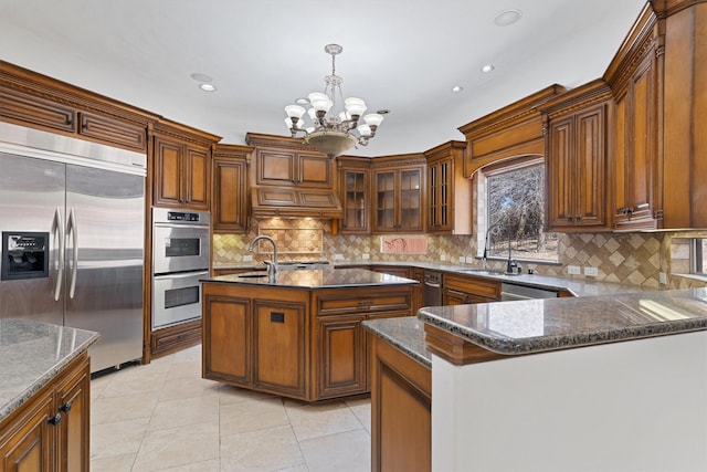 kitchen featuring stainless steel appliances, a sink, hanging light fixtures, backsplash, and dark stone counters