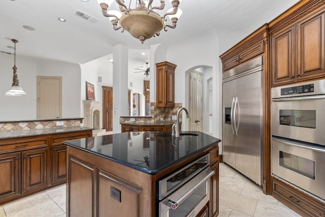 kitchen featuring a kitchen island with sink, appliances with stainless steel finishes, brown cabinetry, and a sink