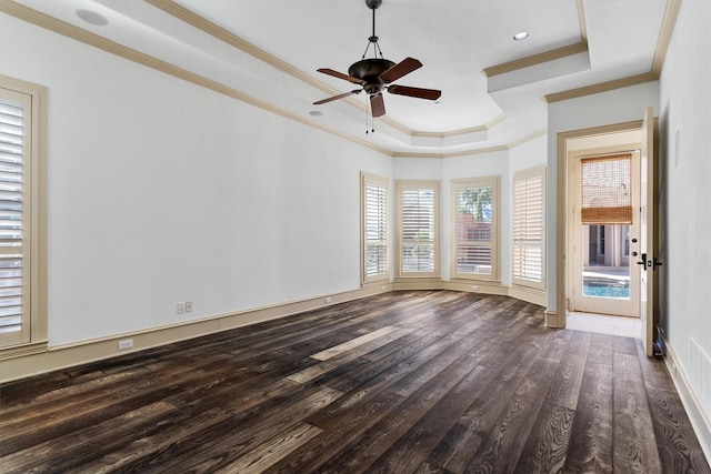 empty room featuring dark wood finished floors, a raised ceiling, ornamental molding, a ceiling fan, and baseboards