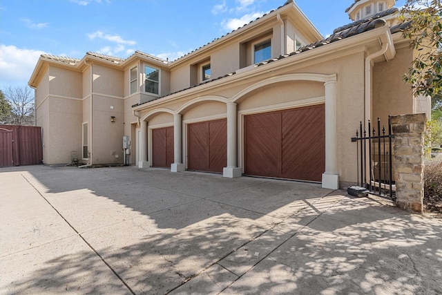 view of front of home with a garage, a tile roof, concrete driveway, a gate, and stucco siding