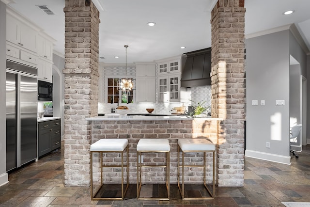 kitchen featuring pendant lighting, ornamental molding, tasteful backsplash, white cabinetry, and built in appliances