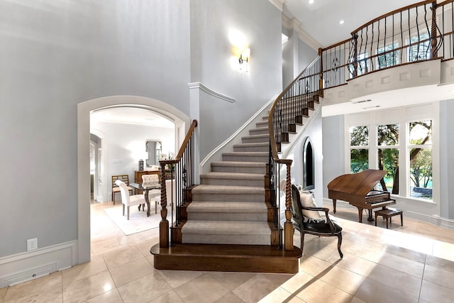 staircase with ornamental molding, tile patterned flooring, and a high ceiling