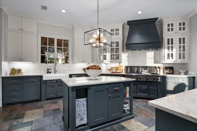 kitchen with hanging light fixtures, white cabinets, backsplash, premium range hood, and sink