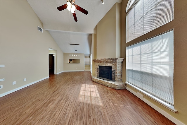 unfurnished living room featuring a brick fireplace, light wood-type flooring, ceiling fan, high vaulted ceiling, and a textured ceiling