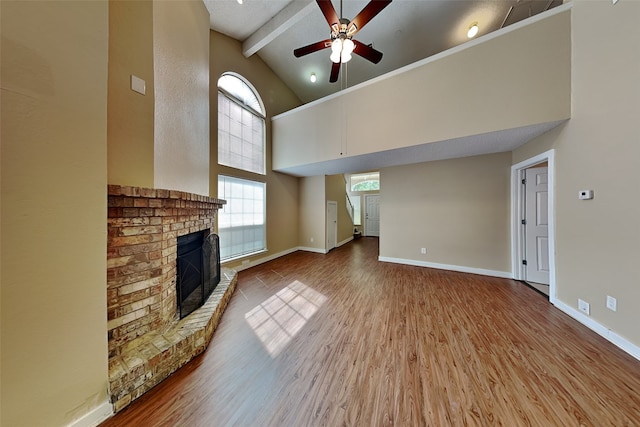 unfurnished living room with beamed ceiling, hardwood / wood-style floors, high vaulted ceiling, a brick fireplace, and ceiling fan