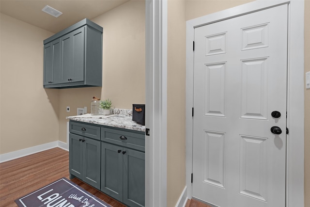 bar featuring dark wood-type flooring, light stone countertops, and gray cabinets