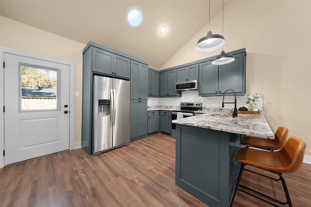 kitchen featuring a kitchen bar, wood-type flooring, kitchen peninsula, light stone countertops, and appliances with stainless steel finishes