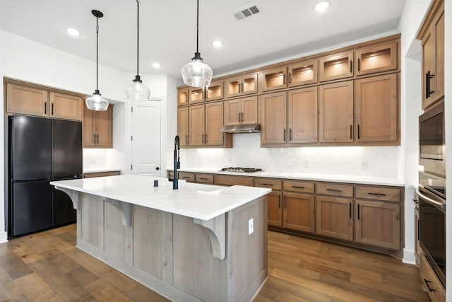 kitchen with appliances with stainless steel finishes, a kitchen island with sink, decorative light fixtures, dark hardwood / wood-style floors, and a breakfast bar area