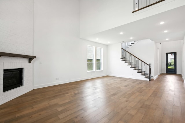 unfurnished living room featuring a fireplace, wood-type flooring, and a high ceiling