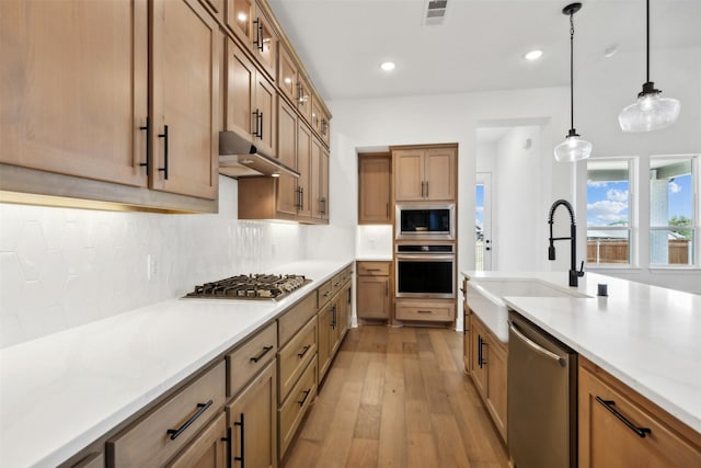 kitchen featuring decorative backsplash, appliances with stainless steel finishes, light wood-type flooring, sink, and pendant lighting