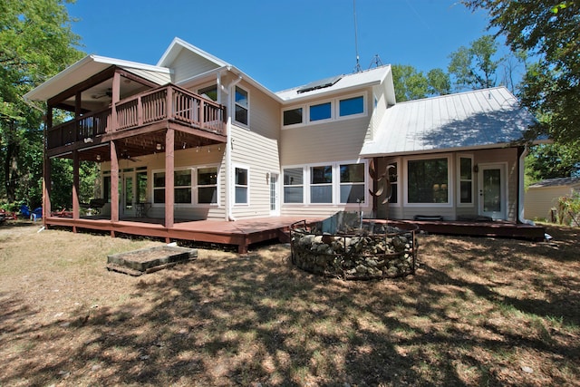 rear view of property featuring ceiling fan, an outdoor fire pit, a lawn, and a wooden deck