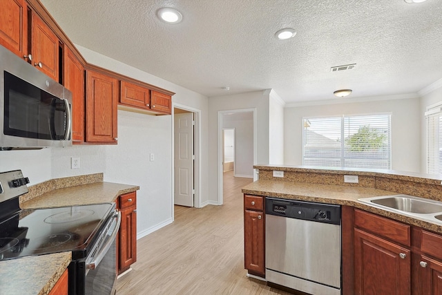 kitchen with light wood-type flooring, appliances with stainless steel finishes, a textured ceiling, and ornamental molding