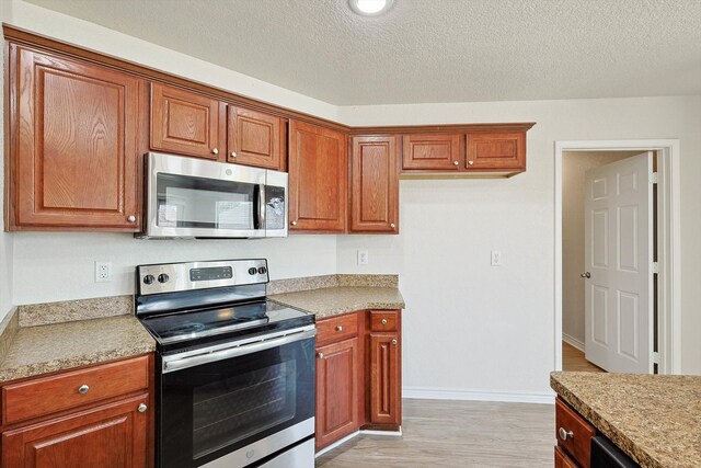 kitchen with appliances with stainless steel finishes, a textured ceiling, and light hardwood / wood-style flooring